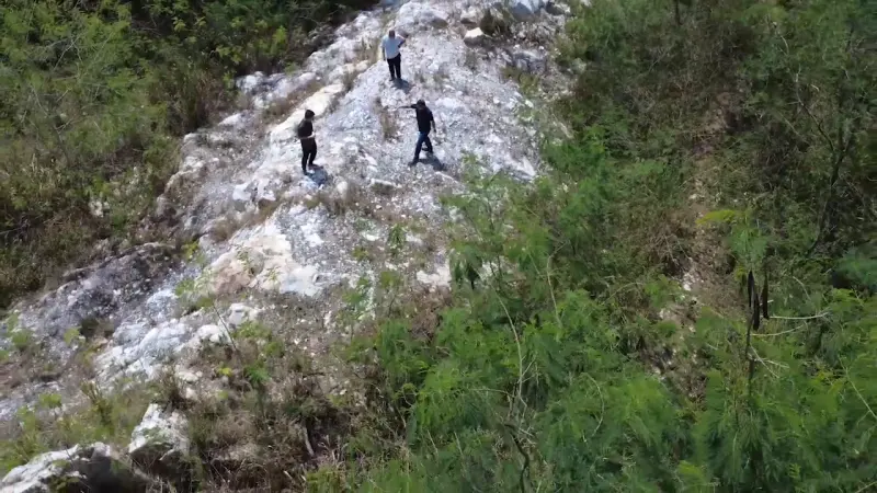 Aerial view of three people walking along a white quartz vein on a wooded hillside
